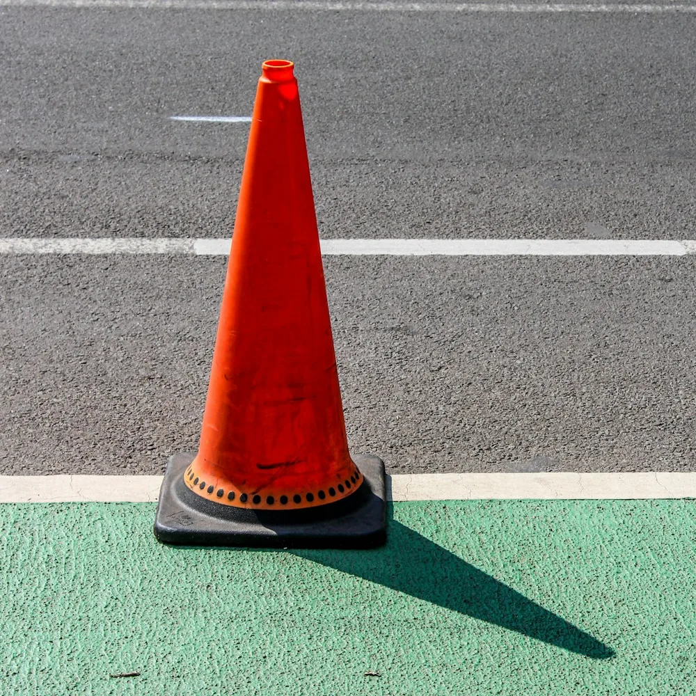 An orange traffic cone standing beside a road