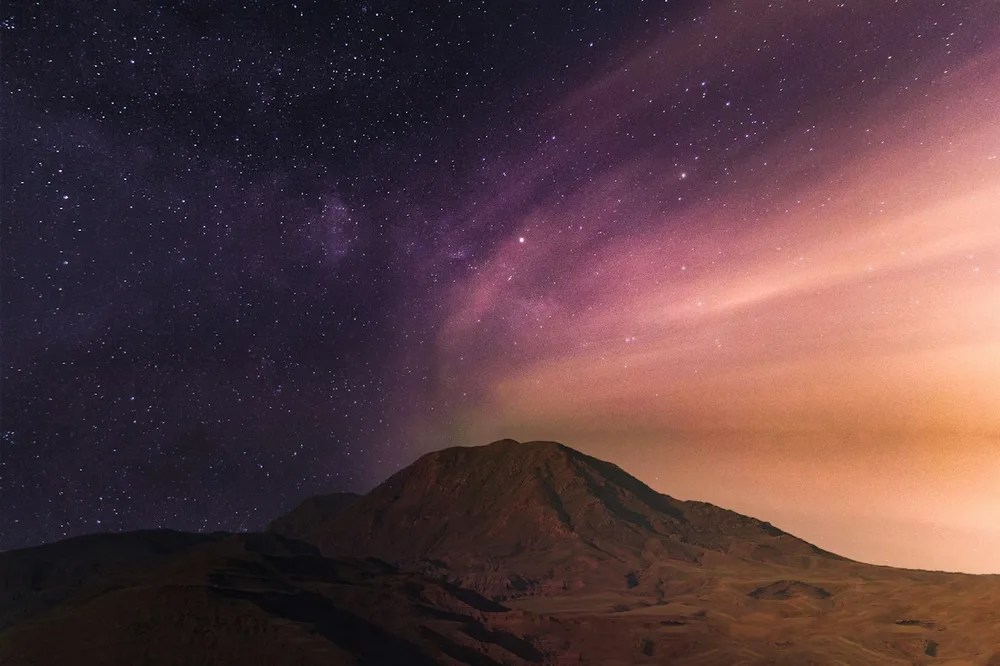 A purple star-filled night sky above a distant mountain horizon